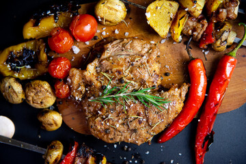 Steak on a wooden cutting board and black background sprinkled with salt and pepper.