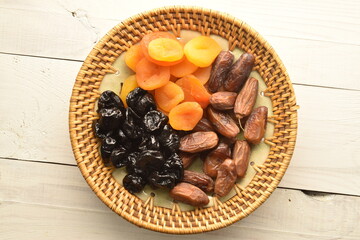 Several appetizing dates, dried apricots, prunes in a ceramic plate on a wooden table, close-up, top view.
