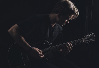 Obraz premium Guy in a T-shirt plays an electric guitar on a dark background