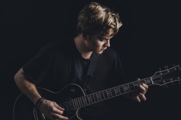Guy in a T-shirt plays an electric guitar on a dark background