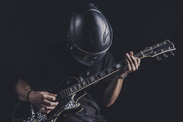 man in motorcycle helmet playing electric guitar on dark background