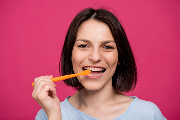Beautiful happy young woman with toothbrush on blank pink background
