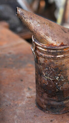 Close-up of smoker for bees. Old rusty bee smoker on metal surface. Beekeeping equipment. Vertical orientation.