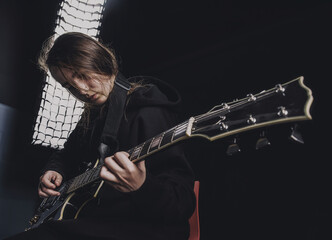 a girl in a black sweatshirt plays an electric guitar on a dark background