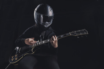 a girl in a black sweatshirt and a motorcycle helmet plays an electric guitar on a dark background