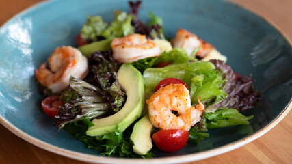 Salad with fresh avocado, lettuce, grilled shrimps, cucumeber on blue dish. Healthy eating. Close up. Selective focus