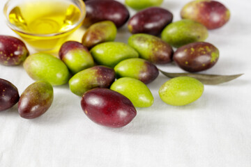 Fresh raw ripe green and black olives and cold pressed oil bowl closeup on linen tablecloth.