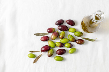 Fresh raw ripe green and black olives and cold pressed oil bottle top view on linen tablecloth.