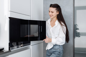 Fototapeta na wymiar Happy woman opening black microwave door in kitchen