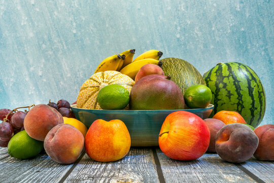 fruits of all kinds on wooden table and striped blue background. Peaches, yellow bananas, ripe watermelons, red apples and grapes, limes and African mangoes.