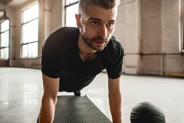 Fototapeta premium Serious man doing plank exercise in gym