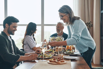 Happy multi-generation family enjoying dinner and smiling while sitting in the modern apartment