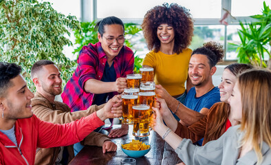 diverse group of friends celebrating happy hour making a toast with pint glasses of beers inside a...