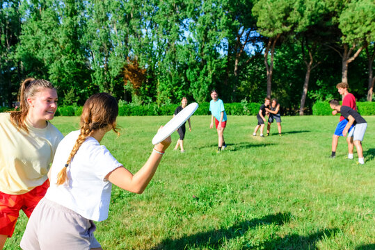 Group of mixed young teenagers people in casual wear playing with flying plastic disk game in a park oudoors. men and women tosses a disc to a teammate in a match. milennial friends outside having fun