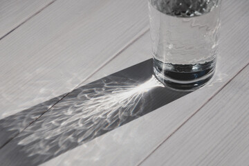 Glass of water on white table in sunlight casting shadow