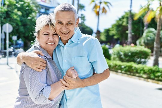Middle age caucasian couple of husband and wife together on a sunny day outdoors. Smiling happy in love hugging at the city.
