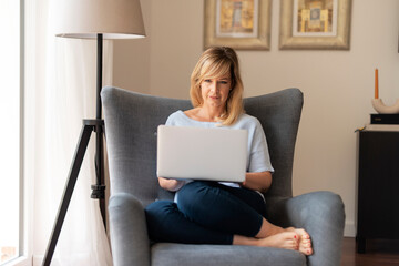 Blond haired woman sitting in the armchair and using laptop at home