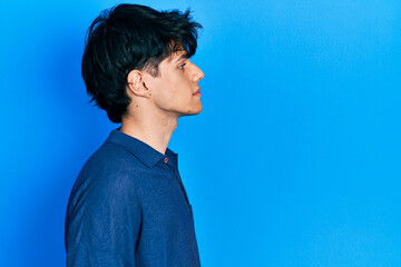 Handsome hipster young man stranding over blue background looking to side, relax profile pose with...
