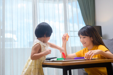 Young mom helping daughter drawing with colored pencils in living room at home.