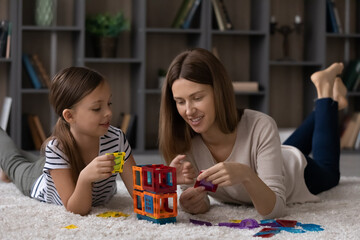 Happy mother and little daughter kid enjoying play on heating floor together, constructing plastic...
