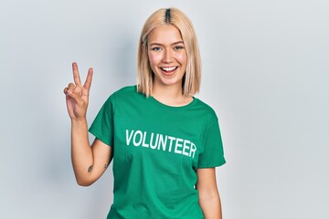 Beautiful blonde woman wearing volunteer t shirt smiling looking to the camera showing fingers...