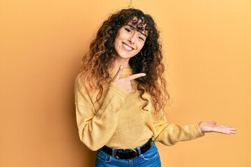 Young hispanic girl wearing casual clothes amazed and smiling to the camera while presenting with hand and pointing with finger.