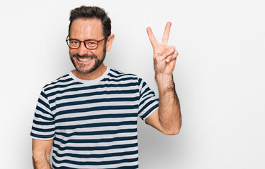 Naklejka premium Middle age man wearing casual clothes and glasses smiling with happy face winking at the camera doing victory sign. number two.