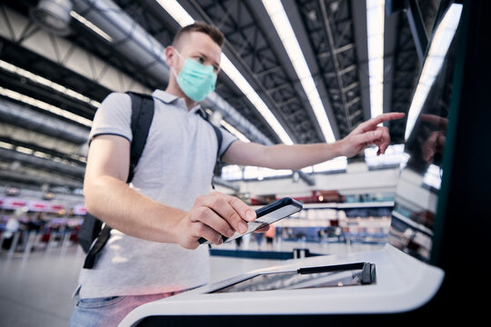 Man using self service check-in machine. Passenger scanning ticket on smart phone at airport terminal. Selective focus on hand holding smartphone..