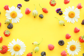 blackberries, gooseberries, raspberries, wild strawberries and strawberries with camomiles on a yellow background. copy space..