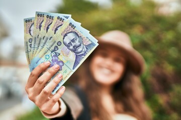 Young hispanic tourist woman smiling happy holding romania lei banknotes at the city.
