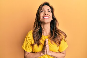 Young latin woman wearing casual clothes begging and praying with hands together with hope...