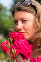 Outdoor photo of romantic young woman in rose garden. Smiling woman posing near blooming roses in park.