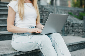 Naklejka premium student girl with laptop sitting on stairs against the background of the university building