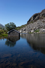 Fototapeta na wymiar Llyn Ogwen, Ogwen lake, with building on the shore in Snowdonia National Park, North Wales. On a summers day with blue sky