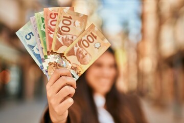 Young hispanic woman smiling happy holding canadian dollars at the city.