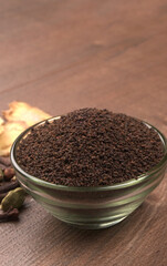Black Tea Powder or dry dust tea powder, chai patti isolated in wooden bowl with Cardamom, Clove and Ginger.
