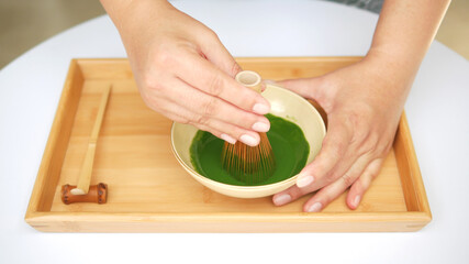 Hands making Japanese organic matcha green tea ceremony by bamboo whisk (chasen) on wooden tray