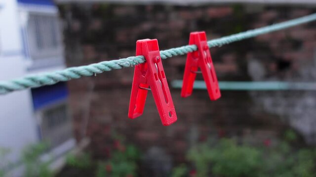 Two red clips hanging on a plastic rope. Clothespins on the rope. Red-colored plastic clothespins on a rope in the environment background. A row of red clothes clips. 4k video.