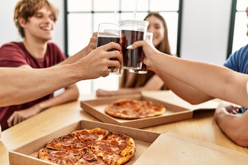 Group of young friends smiling happy eating italian pizza sitting on the table at home.