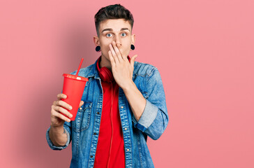 Young caucasian boy with ears dilation drinking glass of cola beverage covering mouth with hand,...