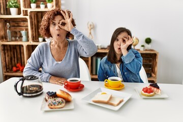 Family of mother and down syndrome daughter sitting at home eating breakfast doing ok gesture shocked with surprised face, eye looking through fingers. unbelieving expression.