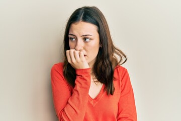 Young brunette woman wearing casual clothes looking stressed and nervous with hands on mouth biting nails. anxiety problem.