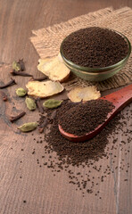 Black Tea Powder or dry dust tea powder, chai patti isolated in wooden bowl with Cardamom, Clove and Ginger.