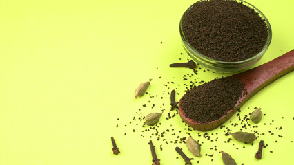 Black Tea Powder or dry dust tea powder, chai patti isolated in wooden bowl with Cardamom, Clove...