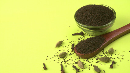 Black Tea Powder or dry dust tea powder, chai patti isolated in wooden bowl with Cardamom, Clove...