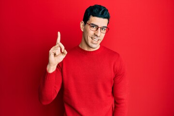 Handsome hispanic man wearing casual clothes and glasses smiling with an idea or question pointing finger up with happy face, number one