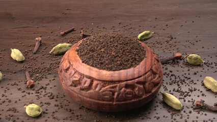 Black Tea Powder or dry dust tea powder, chai patti isolated in wooden bowl with Cardamom, Clove...