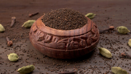 Black Tea Powder or dry dust tea powder, chai patti isolated in wooden bowl with Cardamom, Clove...