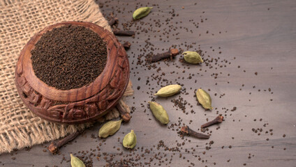 Black Tea Powder or dry dust tea powder, chai patti isolated in wooden bowl with Cardamom, Clove...