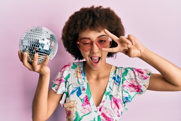 Young hispanic girl wearing summer style holding disco ball winking looking at the camera with sexy...